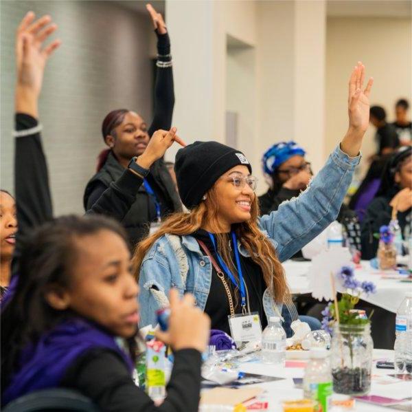 Students raise their hands to be called on while sitting at a table.